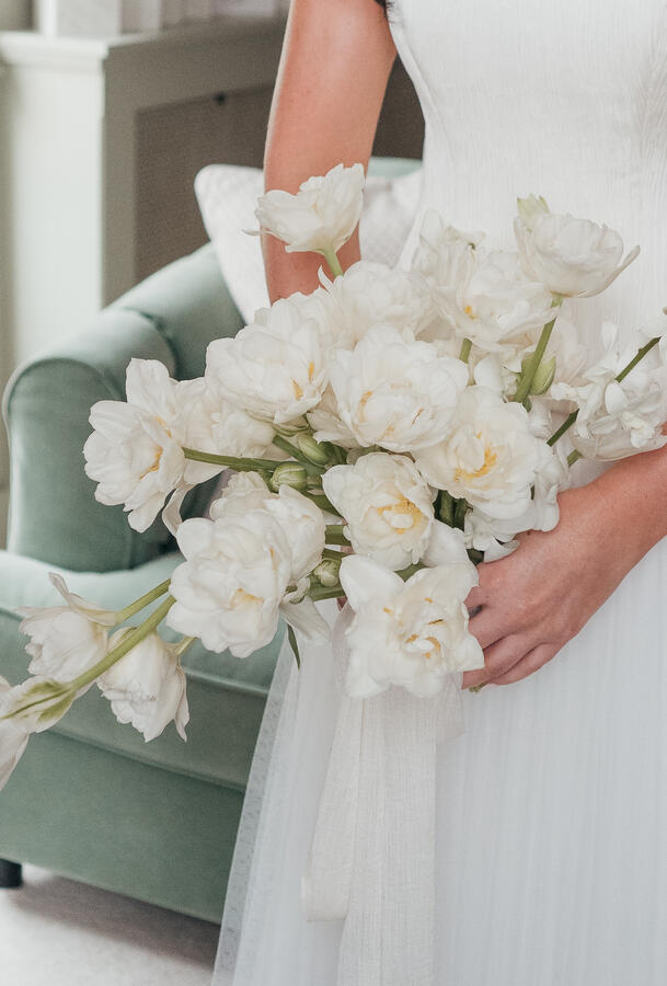 Bridal Bouquet Details Close-up of a bride holding an elegant white wedding bouquet beside her dress.